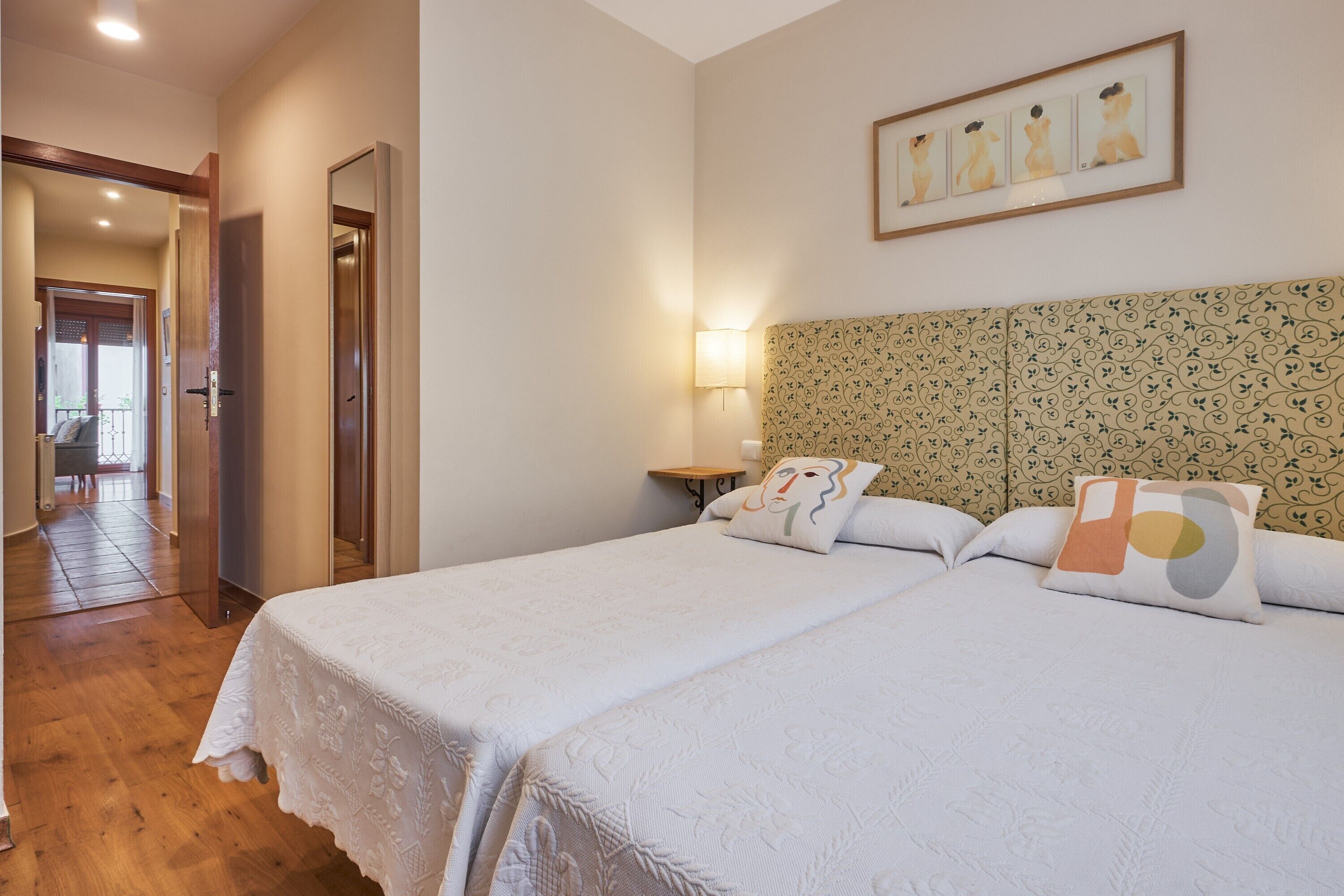 Una habitació d'hotel amb dos llits, un panell de capçalera estampat, una petita taula de nit amb una làmpada i una obra d'art emmarcada penjant sobre el llit.