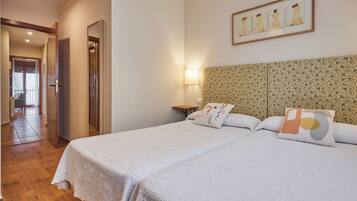 Una habitació d'hotel amb dos llits, un panell de capçalera estampat, una petita taula de nit amb una làmpada i una obra d'art emmarcada penjant sobre el llit.