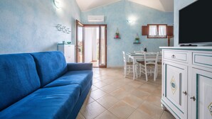 Un salon avec un canapé bleu, un coin repas avec une table et des chaises, et un téléviseur posé sur un meuble.