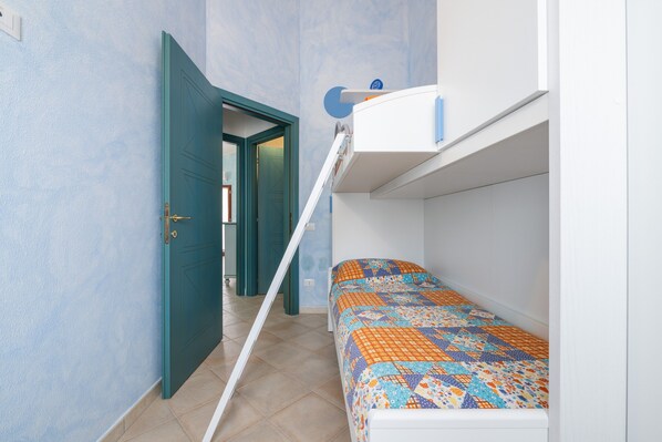 Une pièce avec un lit superposé, une porte donnant sur une autre pièce et une étagère fixée au mur.