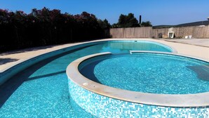 Une piscine dont le bord est revêtu de carreaux, entourée d’une terrasse en béton et d’un petit muret en pierre.