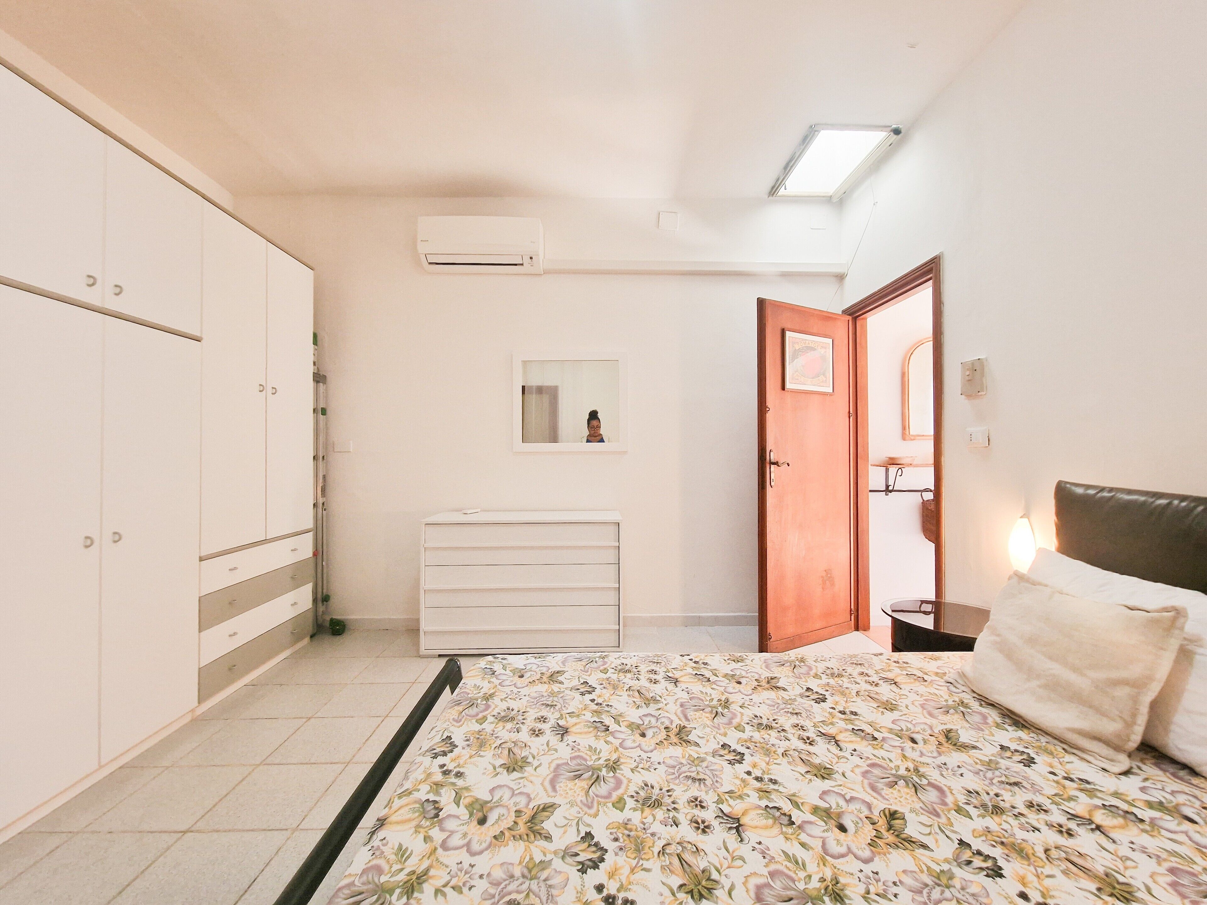 A bedroom with a bed, wardrobe, dresser, and a door leading to another room.
