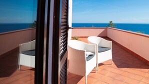 Een balkon met twee witte wickerstoelen, een betegelde vloer en uitzicht op de oceaan.