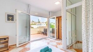 Habitació amb llit, una porta corredissa de vidre que dona a zona exterior, taula petita i cadira.