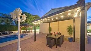 Terrassa exterior amb piscina, zona de menjador coberta i una pergola amb llums penjades.