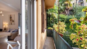 A balcony with a view of lush greenery, a sofa, and a chair. - Studio Apartment 'Kella's Holiday Home' with Balcony, Wi-Fi and Air Conditioning (Bellagio)