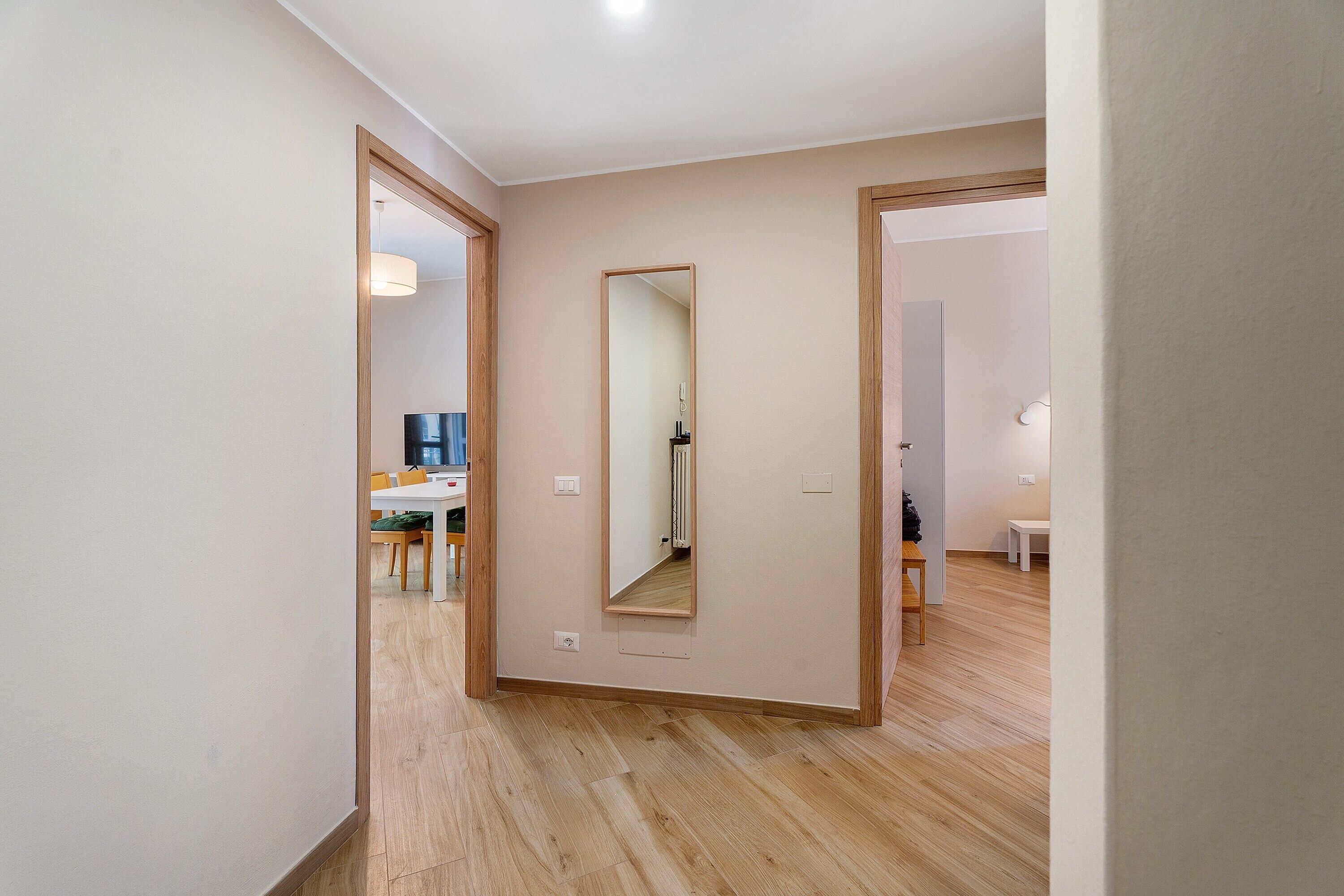 A hallway with wooden flooring, a mirror, and a dining area with chairs and a table.