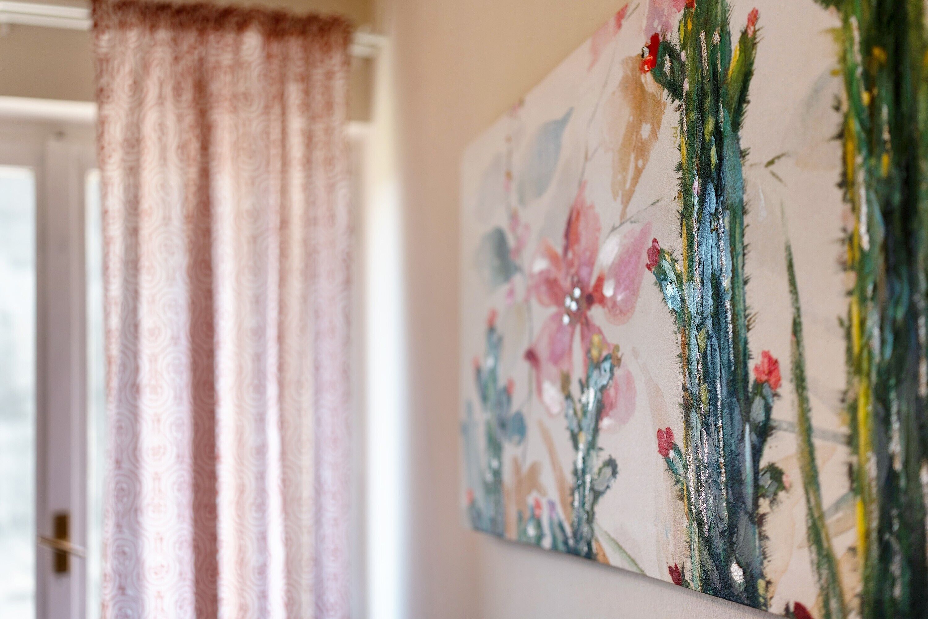 Une pièce avec une porte entrouverte, un rideau et un tableau représentant des fleurs accroché au mur.