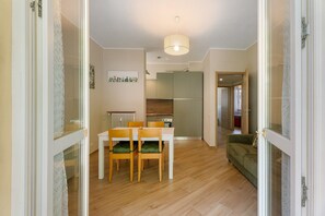 A modern kitchen with a dining area, wooden flooring, and a green sofa.