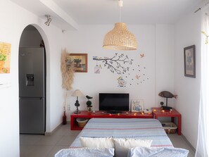 Une chambre à coucher comprenant un lit, un téléviseur, une table de chevet rouge, un mur décoratif et un espace cuisine moderne.