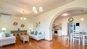 Un vaste espace de vie doté d’un plancher en bois, de meubles blancs et d’une cuisine située à l’arrière-plan.