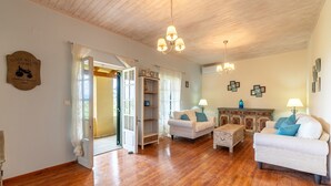 Un salon spacieux doté d’un parquet en bois, de meubles blancs et d’un lustre.