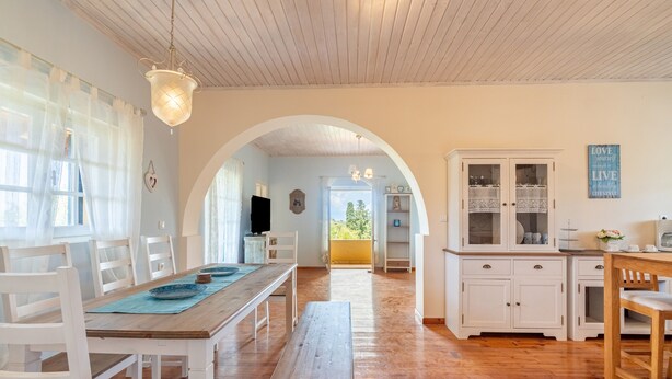Un grand espace à manger avec une table en bois, des chaises blanches et un banc. Il y a également un coin cuisine avec des meubles blancs et un plan de travail en bois.