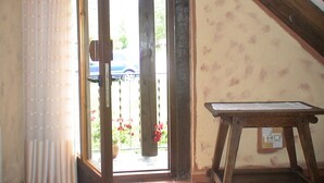 Een kamer met een houten ladder, een raam met uitzicht op een auto en bloemen buiten, en een deur met een gordijn.