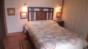 Une chambre à coucher avec un lit, deux lampes fixées au mur, une table de chevet et un tableau encadré accroché au mur.