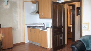 A compact kitchen with wooden cabinets, a built-in microwave, and a tiled floor. - Country House 'Cuarto Del Ama' with Mountain Views, Private Garden and Wi-Fi (Rozas De Sanabria)