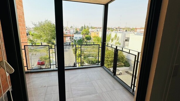 Un balcon donnant sur un quartier résidentiel, une clôture en métal et un sol carrelé.