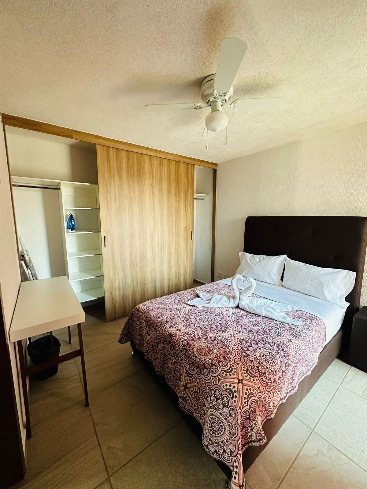 Une chambre d’hôtel équipée d’un lit, d’un bureau, d’une armoire et d’un ventilateur de plafond.