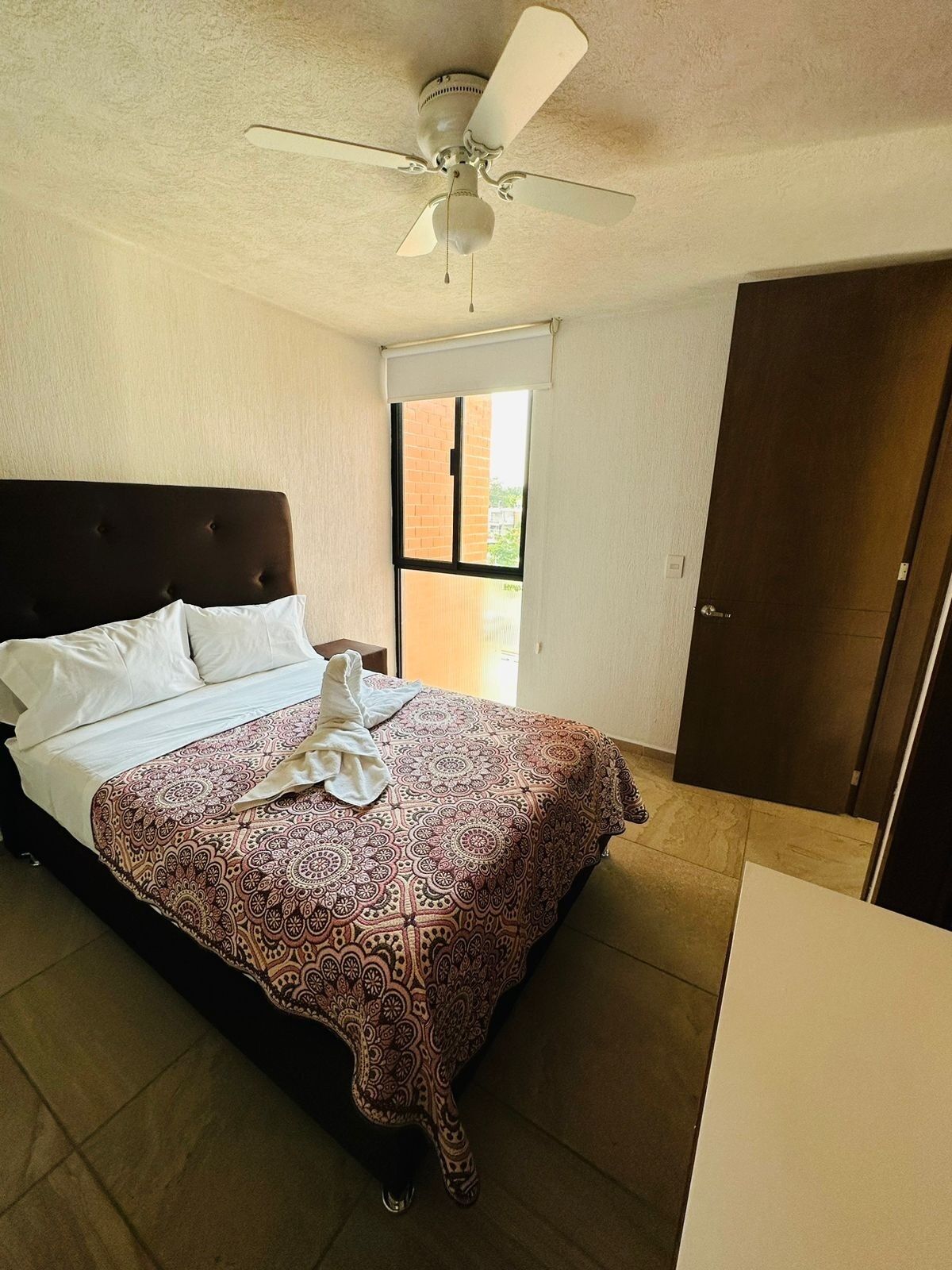 A bedroom with a bed, a ceiling fan, a window, and a door.