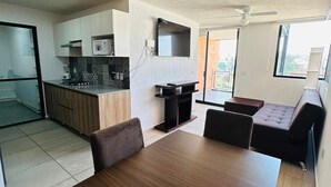 Une cuisine moderne équipée d’un four à micro-ondes, d’une cuisinière et d’un évier. On y trouve également un coin repas avec une table et des chaises en bois. La pièce est dotée d’une grande fenêtre et d’un ventilateur de plafond.