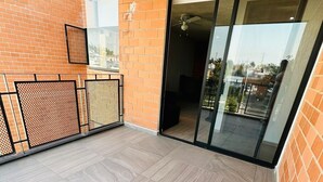 Un balcon doté d’un sol carrelé, d’une rambarde en métal et d’une porte vitrée donnant sur un espace intérieur.