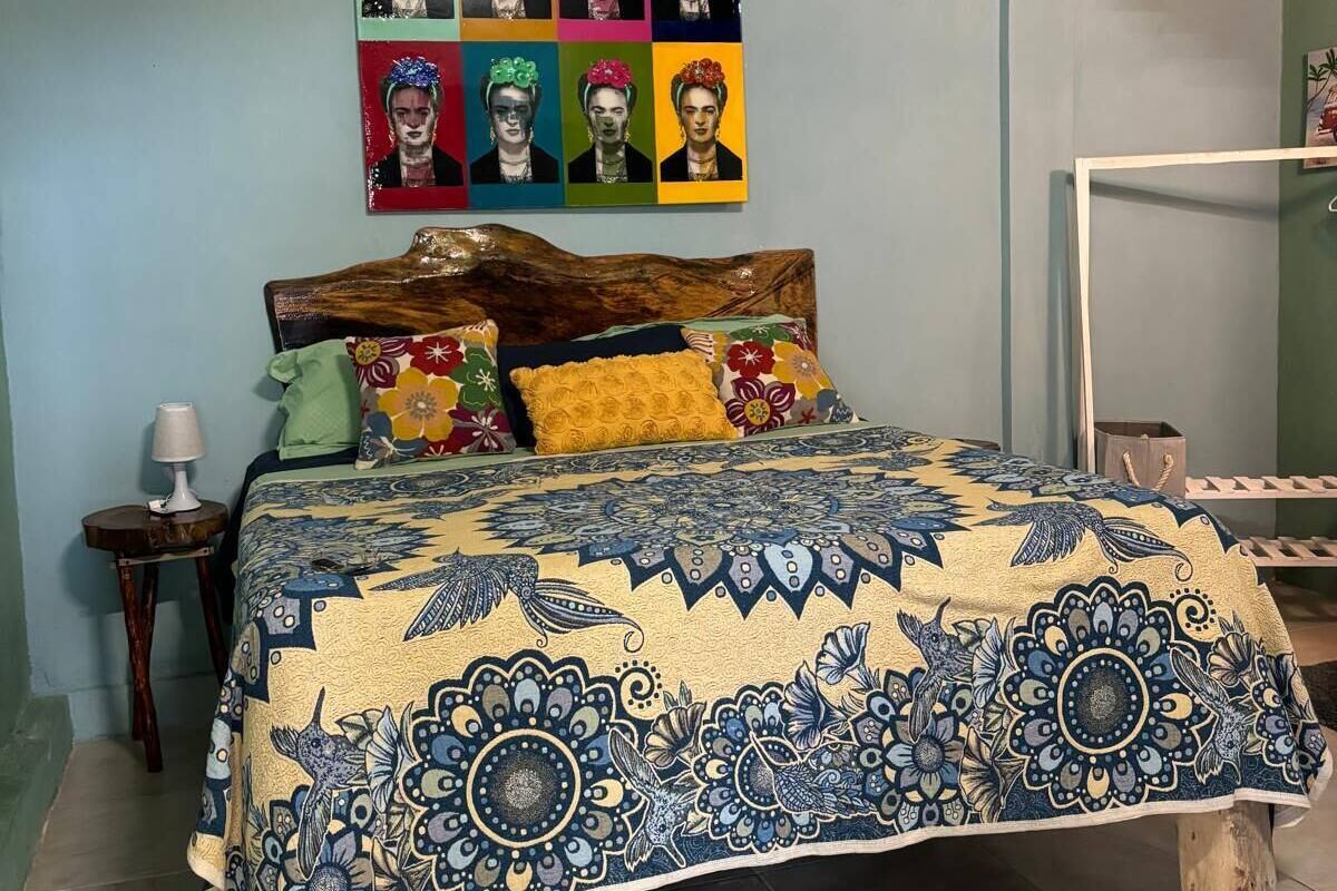 A bedroom with a bed, a wall-mounted air conditioner, a colorful poster, and a wooden headboard.