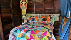 A cozy wooden room with a colorful patchwork bedspread, a woven hanging decoration, and a rustic headboard. - Un Toque de Brazil, Bacalar (Bacalar)