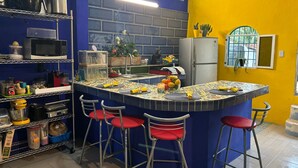 A kitchen with a blue and yellow color scheme, featuring a central island with stools, a refrigerator, and various kitchen appliances. - Un Toque de Brazil, Bacalar (Bacalar)