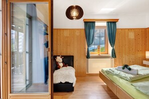 Une pièce avec un lit, une chaise sur laquelle est posé un ours en peluche, une fenêtre avec des rideaux et un luminaire au plafond.