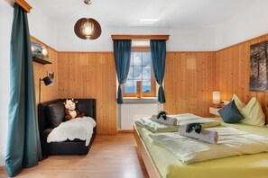A room with a bed, a sofa, a window with curtains, a lamp, and a wall-mounted shelf with a book.