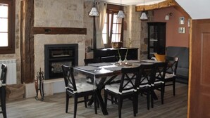 Un coin repas agrémenté d’une cheminée en pierre, de poutres en bois et d’une table dressée pour quatre personnes.