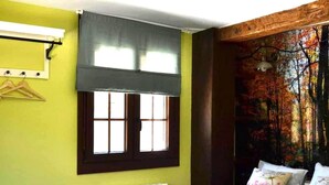 Une chambre à coucher avec un lit, une fenêtre, un radiateur et un mur orné d’une fresque représentant une forêt.
