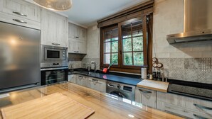 Une cuisine moderne dotée d’appareils électroménagers en acier inoxydable, de meubles de rangement en bois, d’une grande fenêtre et d’une table à manger en verre.
