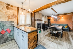 A kitchen with a stone wall, wooden beams, a dining area with a table and chairs, and a fireplace. - Rural House La Genciana with Mountain Views and Wi-Fi in Valmala (Valmala)