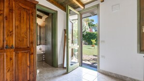 An open wooden door leading to a bathroom with a sink and toilet, a tiled floor, and a view of a garden outside.