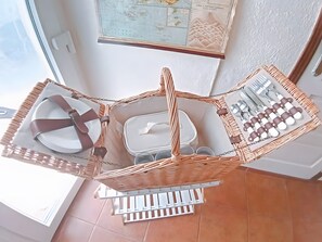 A wicker dining set with plates, cutlery, and a small container, placed on a white stand in a room with a window and a map on the wall. - Holiday Home 'Casalinho Do Chafariz' with Mountain View, Wi-Fi and Air Conditioning (Algaça)