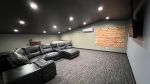 Un cine en casa con sofá modular, piso alfombrado, luces empotradas en el techo y un aire acondicionado de pared.