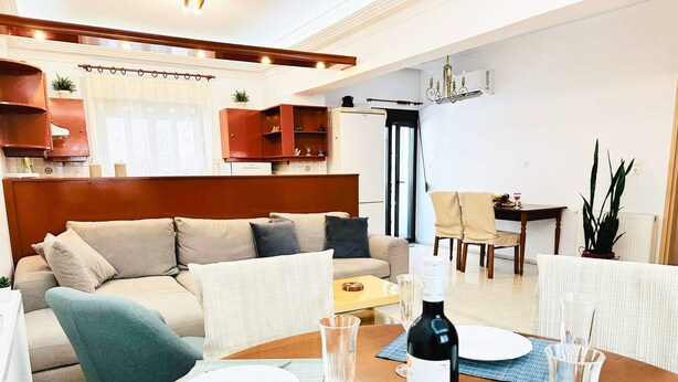 A living room with a sofa, dining table set with plates and wine glasses, and a kitchen area in the background. - Sea Breeze Sanctuary-1bd 3pl 1ba - 90m To Sea (Chania)