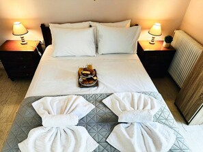 Une chambre d’hôtel avec un lit, deux lampes de chevet, un plateau avec des croissants et du jus, et des serviettes disposées sur le lit.
