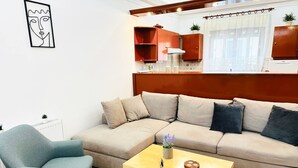A living room with a sofa, a coffee table, a chair, and a kitchen area in the background. - Sea Breeze Sanctuary-1bd 3pl 1ba - 90m To Sea (Chania)
