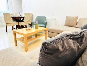 Un salon comprenant un canapé, une table basse, une table à manger avec des chaises et un fauteuil vert.