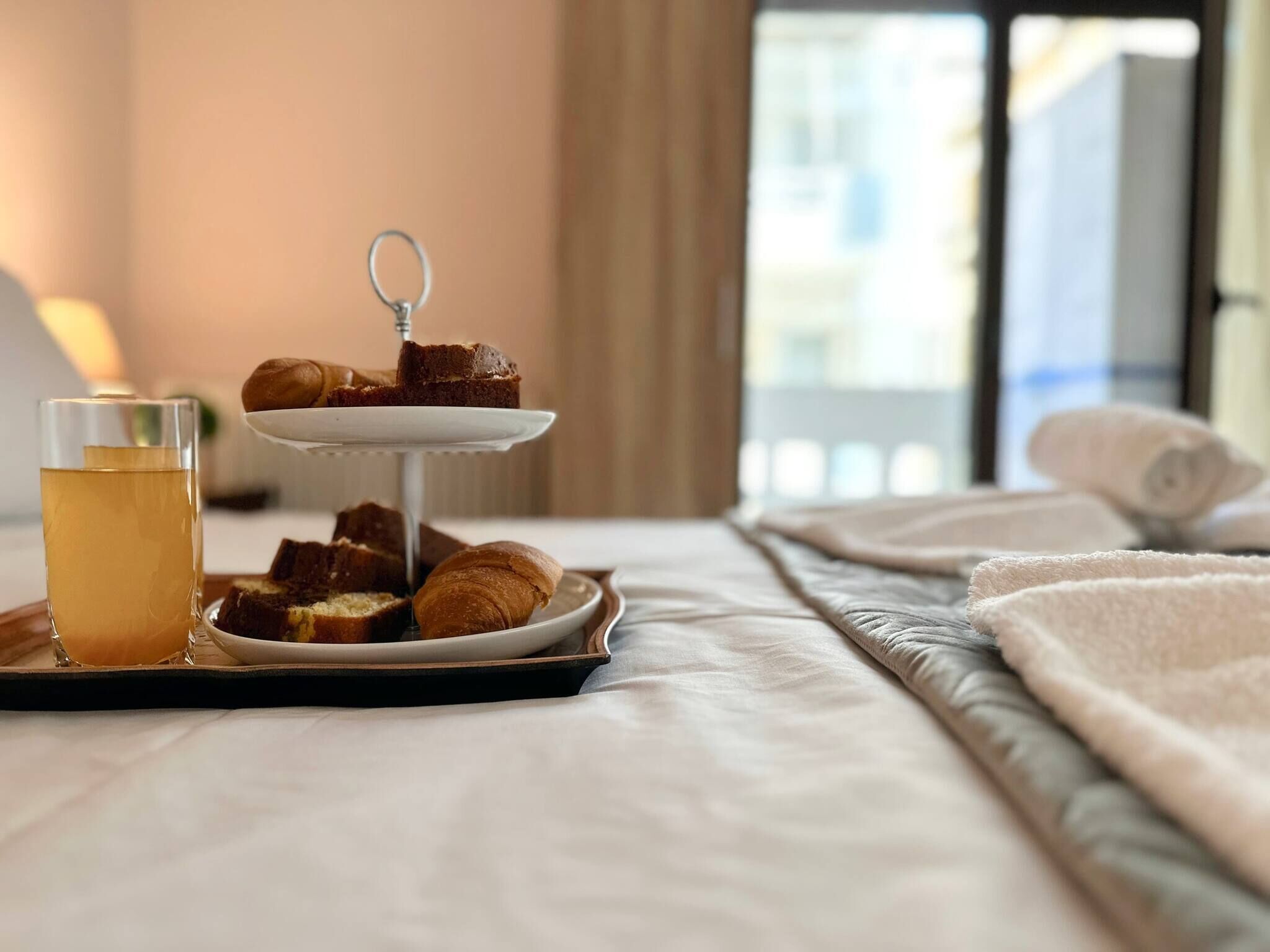 A bed with a tray of food, a glass of tea, and a window view.