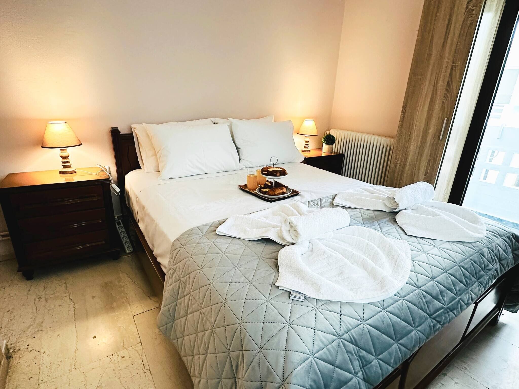 A hotel room with a bed, two bedside lamps, a tray with breakfast items, and a window with curtains.