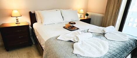 A hotel room with a bed, two bedside lamps, a tray with breakfast items, and a window with curtains.