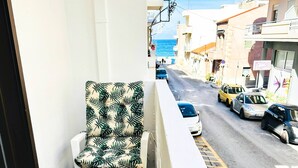A balcony with a chair and table, overlooking a street with parked cars and buildings. - Sea Breeze Sanctuary-1bd 3pl 1ba - 90m To Sea (Chania)