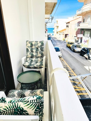 Un balcone con una sedia e un tavolo, affacciato su una strada con auto parcheggiate e palazzi.