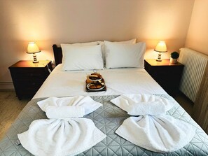 A hotel room with a bed, two bedside tables with lamps, a bedside plant, and towels arranged on the bed. - Sea Breeze Sanctuary-1bd 3pl 1ba - 90m To Sea (Chania)