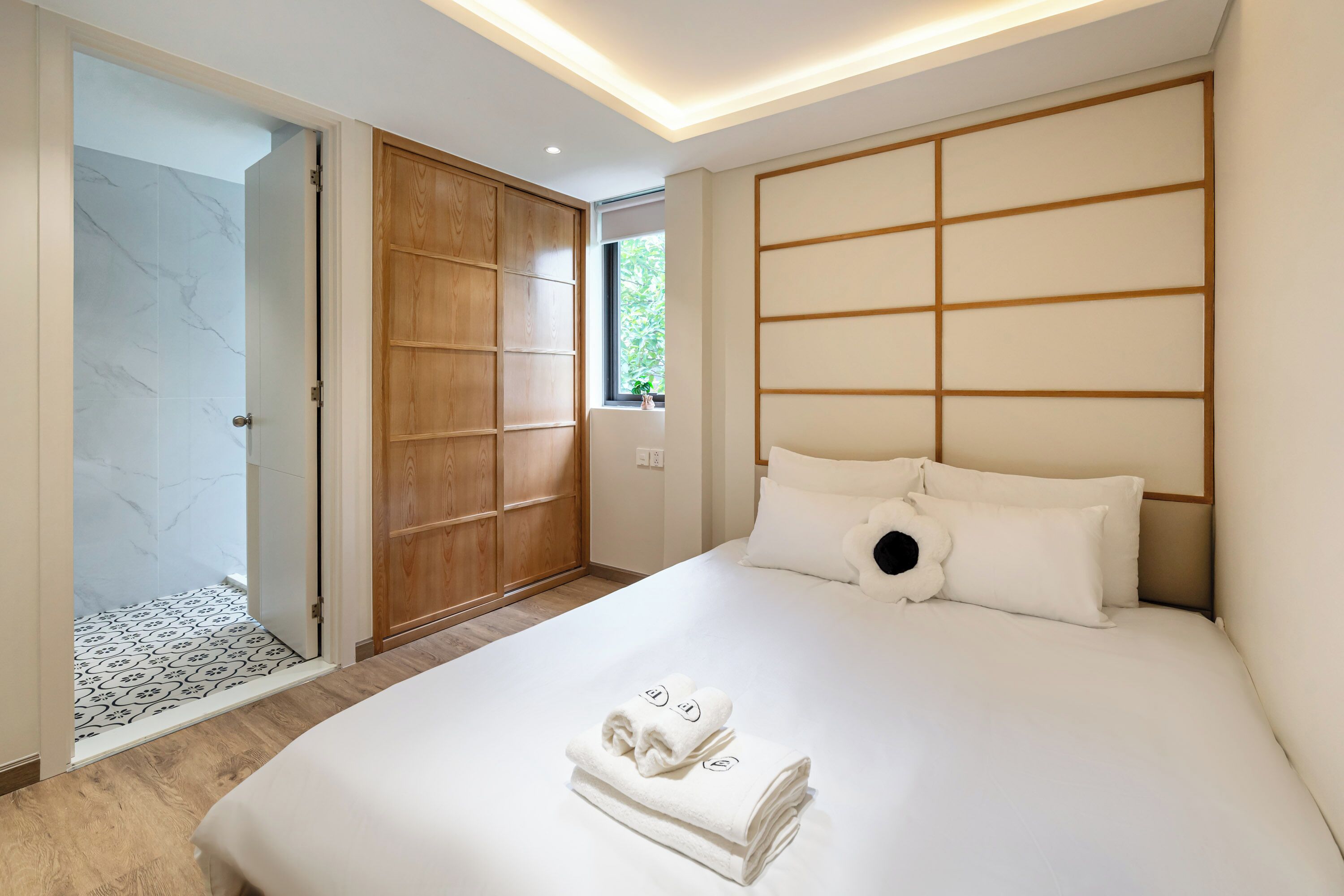 A hotel room with a large bed, a wooden wardrobe, and a bathroom with a patterned floor.