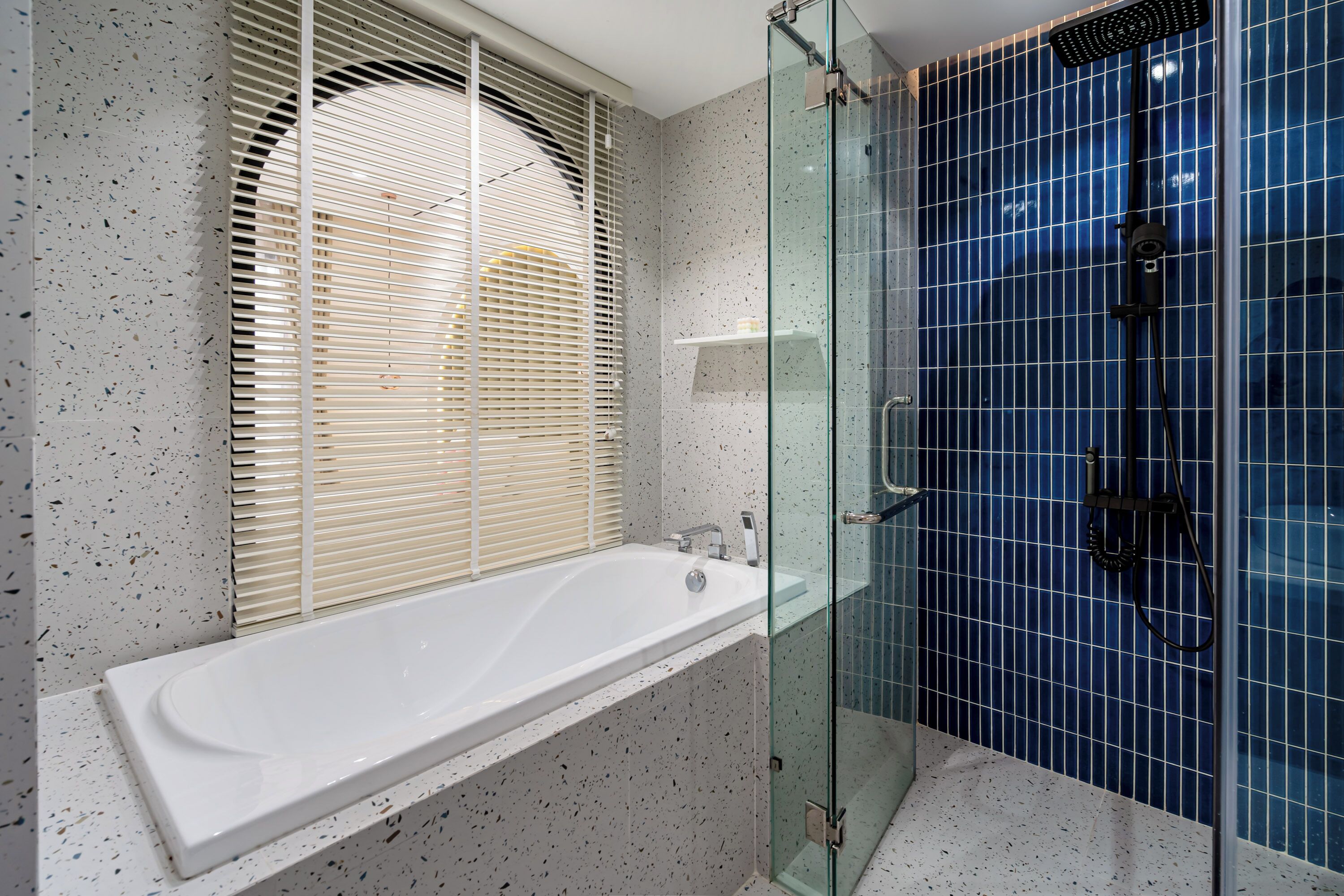 Ein modernes Badezimmer mit einer freistehenden Badewanne, einer begehbaren Glasdusche und einem Fenster mit Jalousien.