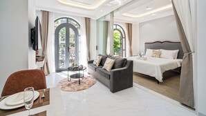 Una habitación de hotel moderna con sofá, una mesa de comedor, cama y ventanas grandes con cortinas.
